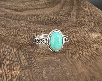 May include: A silver ring with a turquoise stone set in an oval bezel. The ring band is decorated with a Celtic knot design.