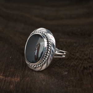 May include: A silver ring with a black oval gemstone set in a rope-like design.