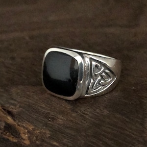 May include: A silver ring featuring a black square stone and a Celtic knot design on the band.