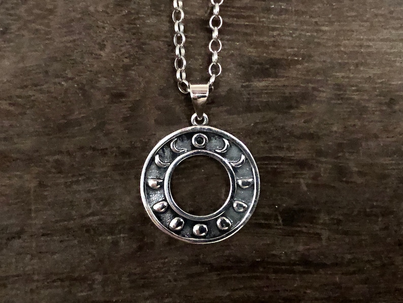 May include: A silver necklace with a circular pendant featuring a detailed design of crescent moons and a sun in the center.