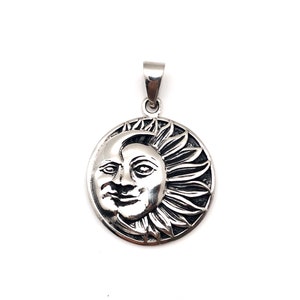 May include: A silver pendant featuring a detailed sun and moon design. The sun is depicted with a face and rays, while the moon is a crescent shape.