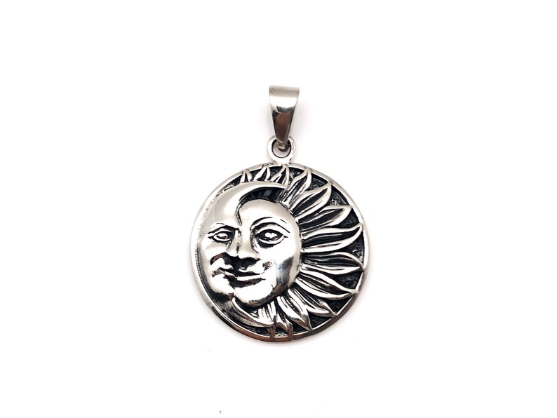 May include: A silver pendant featuring a detailed sun and moon design. The sun is depicted with a face and rays, while the moon is a crescent shape.