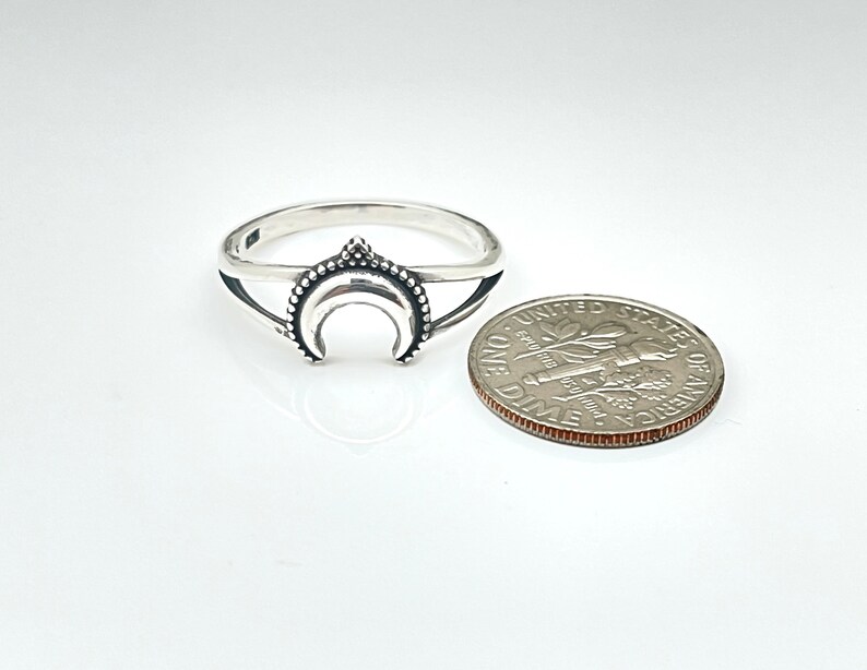 Peut inclure: Une bague argent&eacute;e orn&eacute;e d'un croissant de lune avec une bordure perl&eacute;e. Une pi&egrave;ce de monnaie est &agrave; c&ocirc;t&eacute; de la bague pour comparaison de taille. La bague a un th&egrave;me c&eacute;leste.