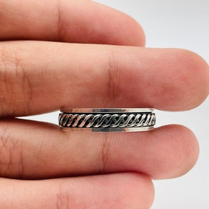 May include: A silver ring with a braided design. The ring is worn on a finger.