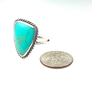 May include: A turquoise ring with a silver setting. The ring is in the shape of a triangle and has a rope-like design around the edge. The ring is next to a US dime for size comparison.