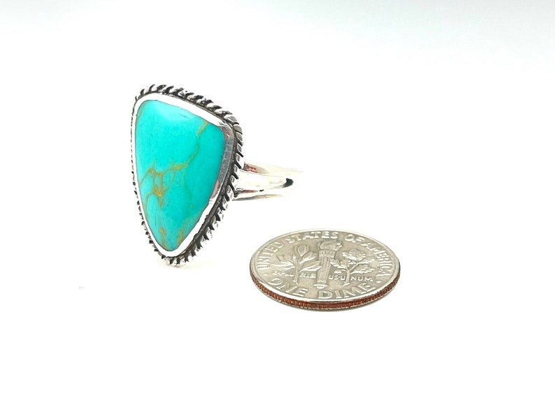 May include: A turquoise ring with a silver setting. The ring is in the shape of a triangle and has a rope-like design around the edge. The ring is next to a US dime for size comparison.