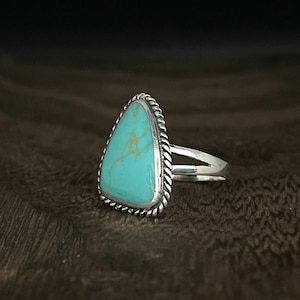 May include: A silver ring with a triangular turquoise stone set in a rope-like border.