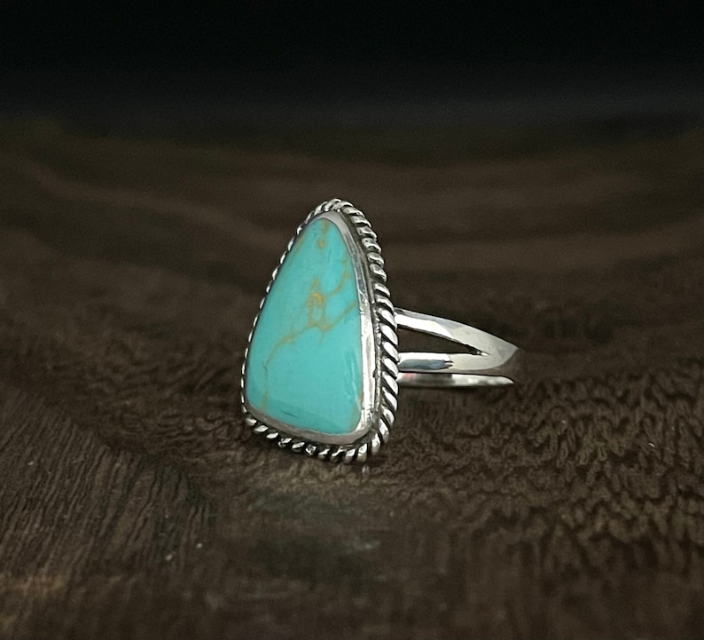 May include: A silver ring with a triangular turquoise stone set in a rope-like border.