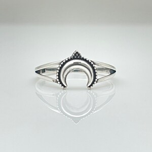 Peut inclure: Bague argent&eacute;e orn&eacute;e d'un croissant de lune. La bague pr&eacute;sente un croissant de lune d&eacute;taill&eacute; avec une bordure perl&eacute;e et un petit triangle au sommet. L'anneau est divis&eacute;, cr&eacute;ant un look unique et &eacute;l&eacute;gant.