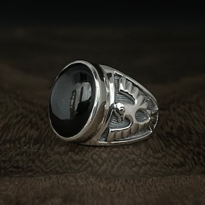 May include: A silver ring with a black oval gemstone and a detailed bird design on the band.