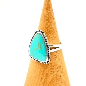 May include: A silver ring with a turquoise stone set in a triangular shape. The ring has a rope-like design around the edge of the stone.