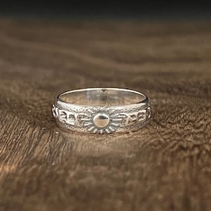 May include: A silver ring with a sun design and a textured band.