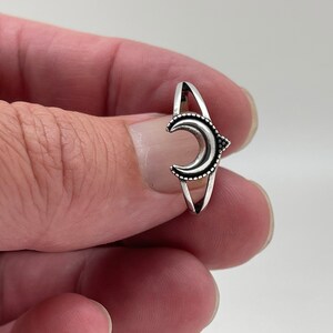 Peut inclure: Une bague argent&eacute;e orn&eacute;e d'un croissant de lune. La lune est orn&eacute;e d'une bordure pointill&eacute;e et se trouve entre deux bandes parall&egrave;les. La bague a un th&egrave;me minimaliste et c&eacute;leste.