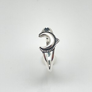 Peut inclure: Une bague argent&eacute;e orn&eacute;e d'un croissant de lune. La lune est orn&eacute;e de petits ornements ronds sur ses bords et d'une surface textur&eacute;e. La bague a une esth&eacute;tique &eacute;l&eacute;gante et moderne.