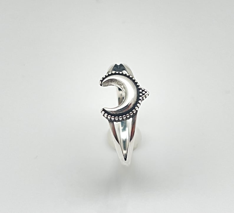 Peut inclure: Une bague argent&eacute;e orn&eacute;e d'un croissant de lune. La lune est orn&eacute;e de petits ornements ronds sur ses bords et d'une surface textur&eacute;e. La bague a une esth&eacute;tique &eacute;l&eacute;gante et moderne.