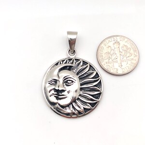 May include: Silver pendant featuring a detailed sun and moon design. The sun has a face and rays, while the moon is a crescent shape. The pendant is about the size of a dime.