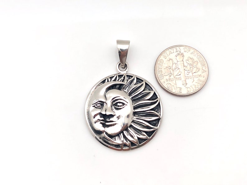 May include: Silver pendant featuring a detailed sun and moon design. The sun has a face and rays, while the moon is a crescent shape. The pendant is about the size of a dime.