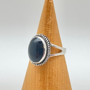 May include: A silver ring featuring a black oval gemstone set in a decorative silver bezel. The ring has a simple band with a split shank.