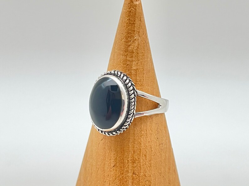 May include: A silver ring featuring a black oval gemstone set in a decorative silver bezel. The ring has a simple band with a split shank.
