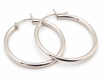 May include: A pair of polished silver hoop earrings with a smooth, rounded profile. Each earring features a hinged post mechanism that secures the circular band, showcasing a reflective metallic finish and a simple, continuous design.