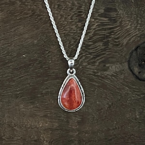 May include: A silver chain necklace with a teardrop-shaped pendant featuring a red and orange stone.