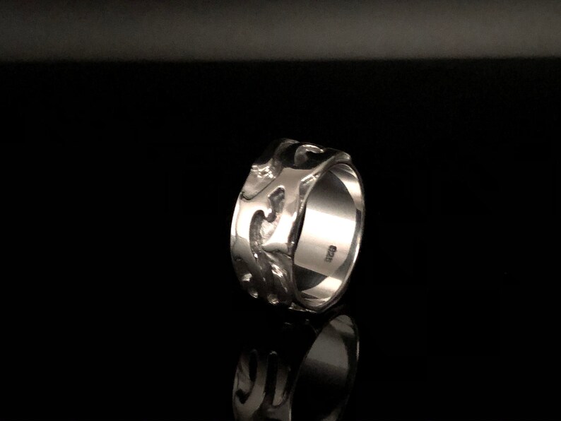 May include: A silver ring with a textured, wave-like design. The ring is wide and has a polished finish.
