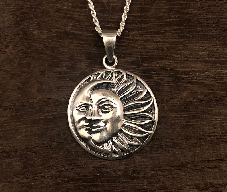 May include: A silver pendant necklace featuring a detailed sun and moon design. The sun has a face and rays, while the moon is a crescent shape.