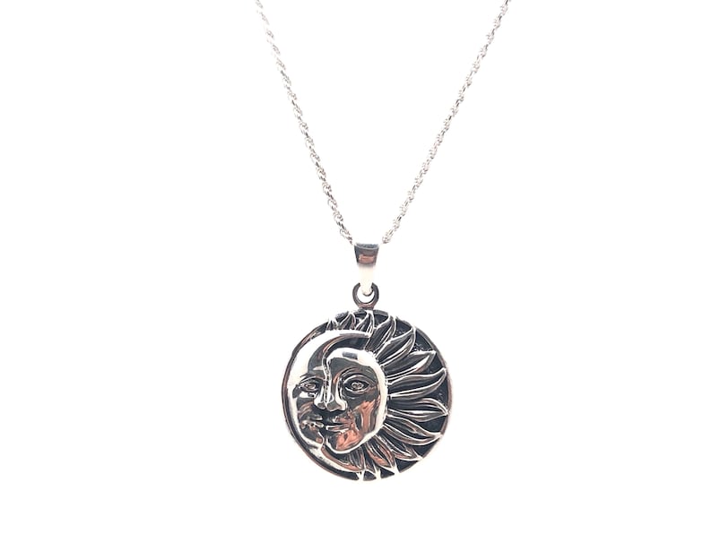 May include: A silver necklace with a round pendant featuring a detailed design of a sun and moon.