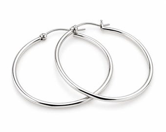 May include: A pair of polished silver-tone hoop earrings featuring a smooth, circular design with a hinged post closure. The earrings have a reflective metallic finish and a simple, continuous round shape that overlaps slightly in the center.