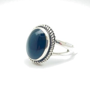 May include: A silver ring featuring a black oval gemstone set in a decorative silver bezel. The ring has a simple band.