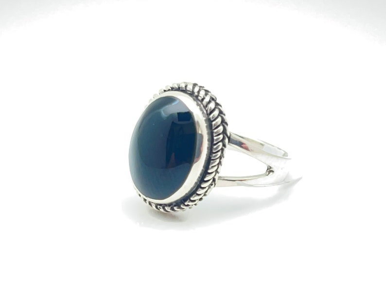 May include: A silver ring featuring a black oval gemstone set in a decorative silver bezel. The ring has a simple band.