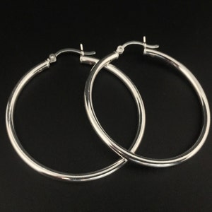 May include: A pair of silver hoop earrings. The hoops are thick and round, and they are made of a smooth metal.