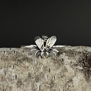 May include: A silver ring featuring a detailed fly design. The fly is facing forward with its wings outstretched.