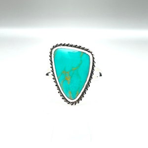May include: A turquoise ring with a silver setting. The turquoise is a triangular shape with a light blue color and brown veins.