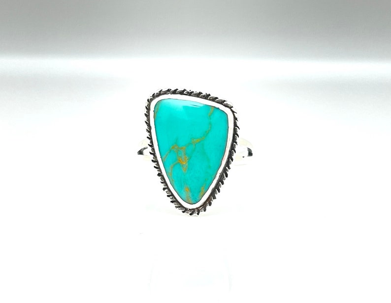May include: A turquoise ring with a silver setting. The turquoise is a triangular shape with a light blue color and brown veins.