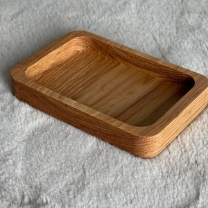 May include: A rectangular wooden tray with a smooth, slightly rounded interior. The tray is made of light brown wood with a natural grain pattern.