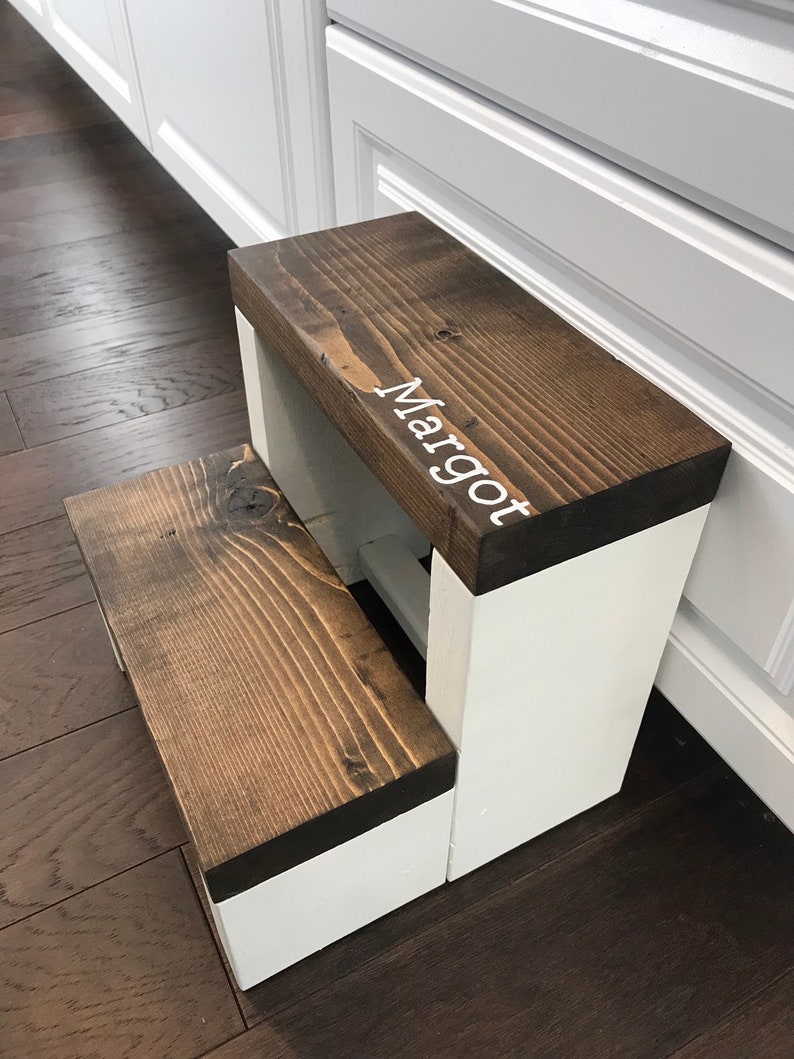 Large wooden step stool, dark walnut stained steps with white painted supports, personalized name hand painted on step, step stool in a kitchen, step stool against cabinet, kids step stool, modern style