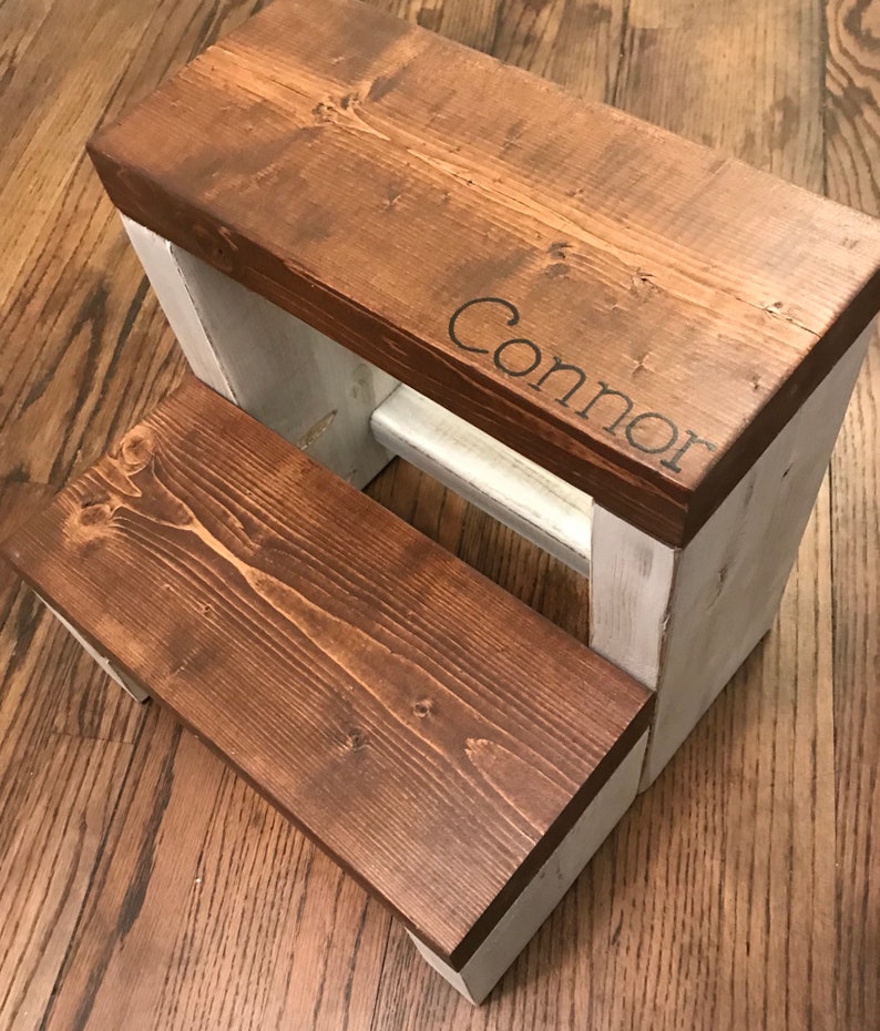 Large wooden step stool, dark walnut stained steps with rustic white painted supports, personalized name hand painted on step, step stool in a kitchen, step stool against cabinet, kids step stool, modern style