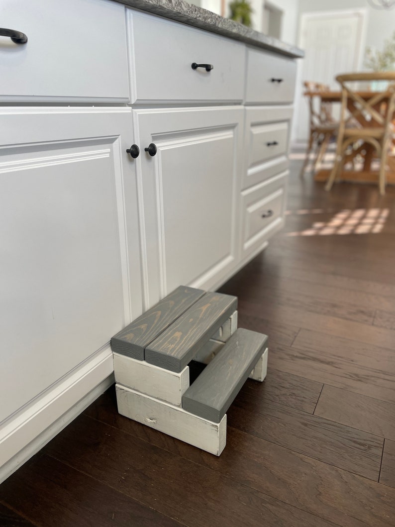 Wooden step stool, weathered gray stained steps with rustic white painted supports, personalized name hand painted on step, step stool in a kitchen, step stool in dining area, step stool against cabinet, kids step stool, adult weight