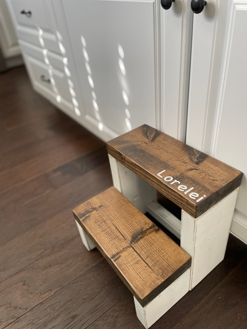 Large wooden step stool, dark walnut stained steps with rustic white painted supports, personalized name hand painted on step, step stool in a kitchen, step stool against cabinet, kids step stool, modern style