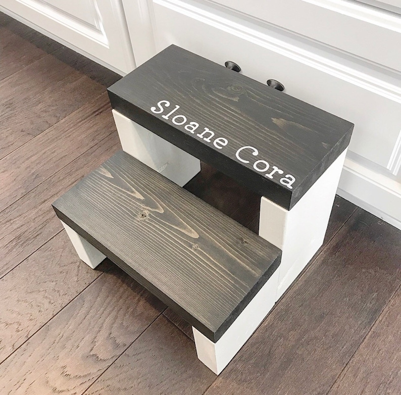 Wooden step stool, ebony stained steps with white painted supports, personalized name hand painted on step, step stool in a kitchen, step stool against cabinet