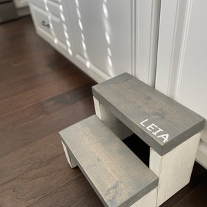 Wooden step stool, weathered gray stained steps with rustic white painted supports, personalized name hand painted on step, step stool in a kitchen, step stool against cabinet