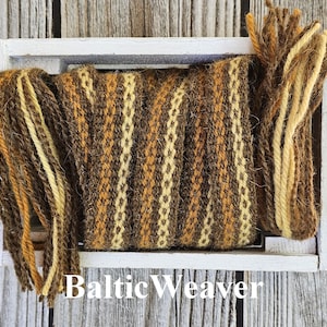 Op de afbeelding: Een geweven wollen band in bruin, geel en wit in een witte houten doos. De band is gemaakt van meerdere samen geweven garenstrengen. De tekst "Baltic Weaver" is afgedrukt op de onderkant van de doos.