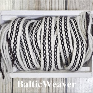 Op de afbeelding: Een zwart-wit geweven textiel is opgerold in een witte houten kist. Het textiel heeft een herhalend patroon van zwarte in elkaar grijpende vormen op een witte achtergrond. De tekst "Baltic Weaver" is zichtbaar aan de onderkant.