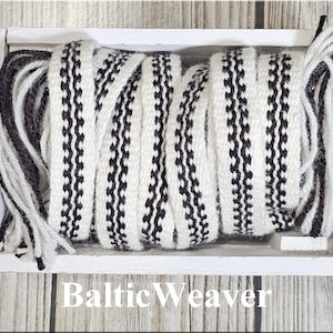 Op de afbeelding: Een witte houten bak gevuld met een geweven textiel. Het textiel is wit met een herhalend zwart zigzagpatroon. De tekst "Baltic Weaver" staat onderaan de afbeelding. Het textiel wordt waarschijnlijk gebruikt voor knutselen of decoratie.