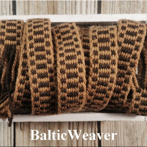 Op de afbeelding: Bruin en zwart geweven lint met een geruit patroon. Het lint wordt getoond op een wit oppervlak met de tekst "Baltic Weaver" eronder.