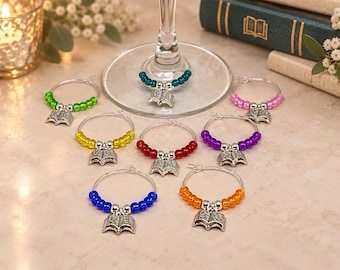 May include: A set of eight circular wine glass charms, each featuring a silver-toned open book charm and a row of colorful beads. The beads are available in green, yellow, red, blue, orange, purple, pink, and teal, with silver spacers.