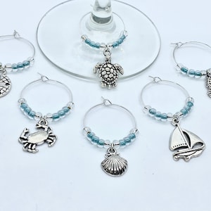 May include: Set of six silver-tone glass charms with blue beads. Each charm features a different sea creature: a starfish, crab, turtle, seashell, sailboat, and seahorse.