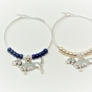 May include: Two silver wine glass charms with dachshund charms. One charm has blue beads and the other has gold beads.