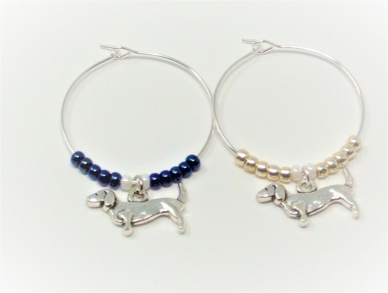 May include: Two silver wine glass charms with dachshund charms. One charm has blue beads and the other has gold beads.